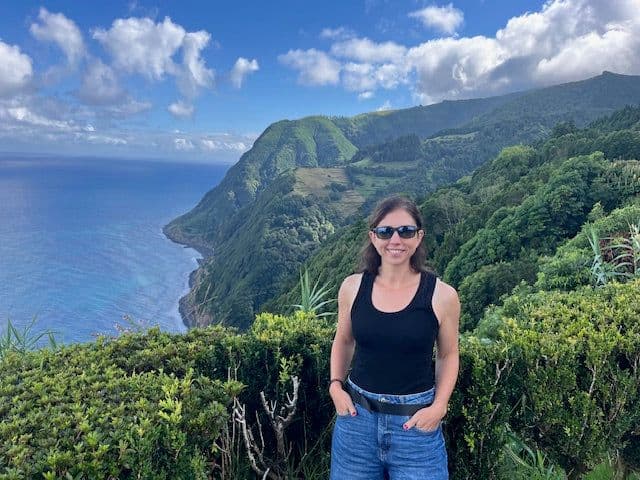 Jenn Pavicich at a lookout above a green coastline and the ocean